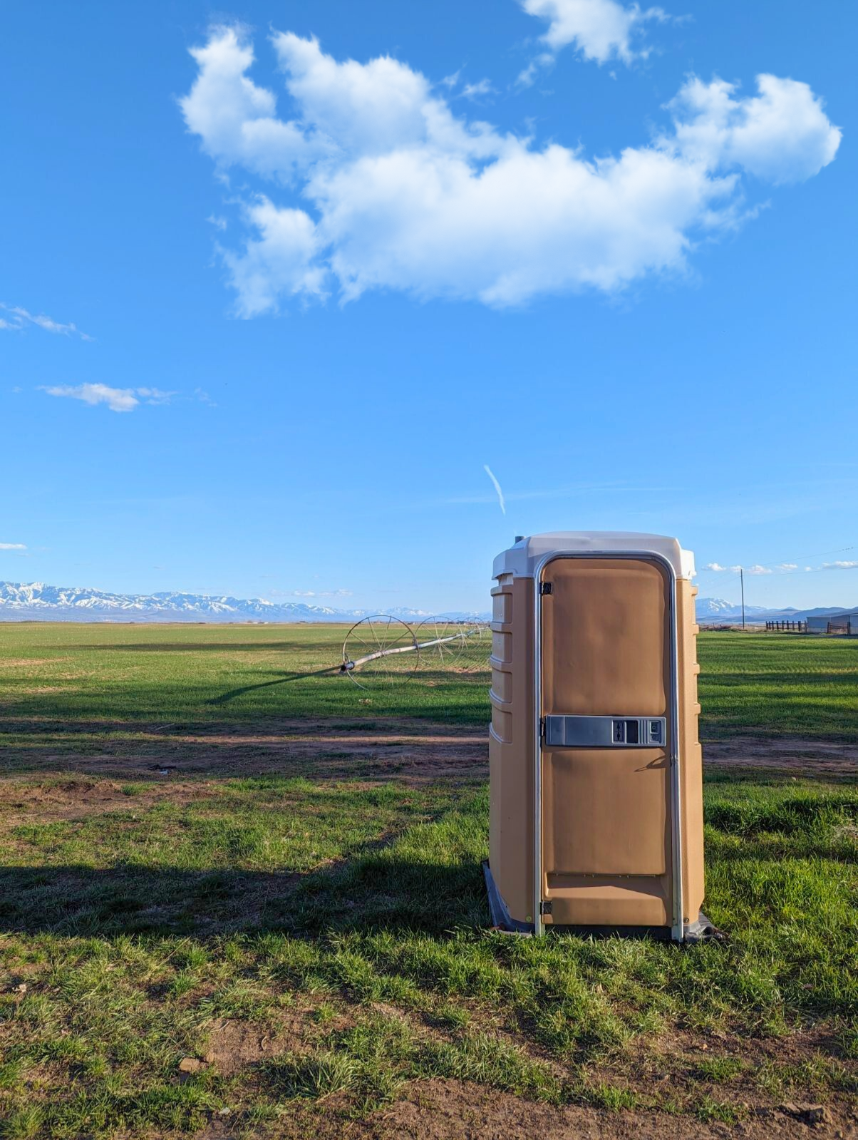 Portable toilet beside an open field under a blue sky